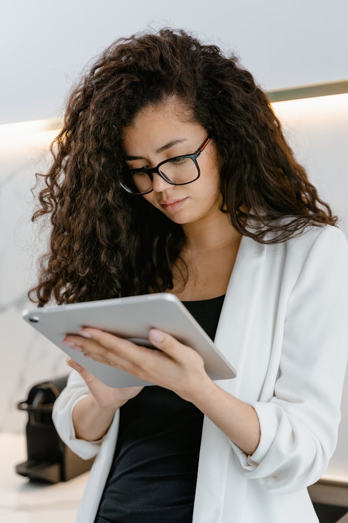 Woman with eyeglasses using a tablet in a modern indoor setting.